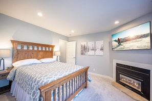 A bedroom with a wooden headboard, a large bed, a fireplace, and wall art.