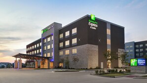Un bâtiment de la chaîne Holiday Inn Express & Suites, doté d’un design moderne, avec une entrée imposante et un espace extérieur couvert.