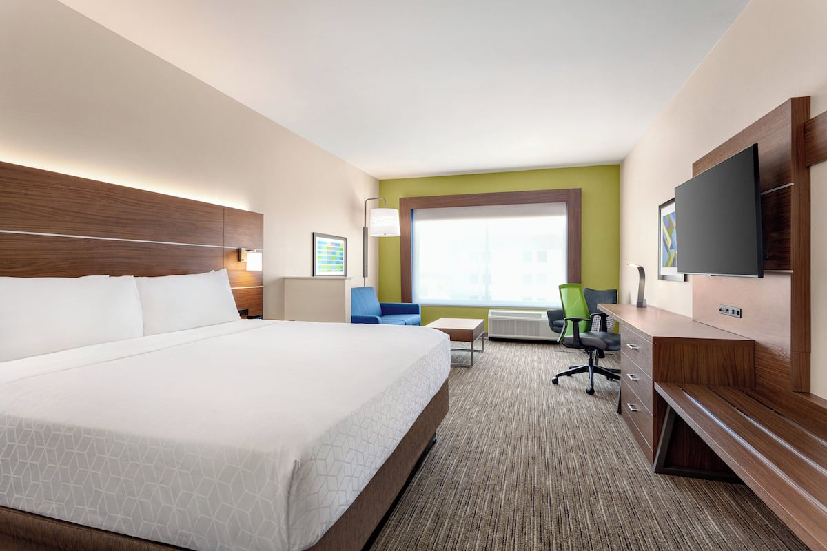 A hotel room with a large bed, a desk, a chair, a television, and a window.