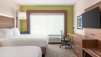 A hotel room with two beds, a desk, a chair, a TV, and a window with blinds.
