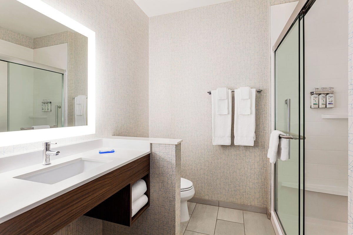 A modern bathroom with a large mirror, a sink, a toilet, and a glass shower enclosure.