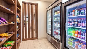 Un espace dédié aux collations et aux boissons, avec des étagères remplies de divers en-cas et un réfrigérateur contenant une variété de boissons.