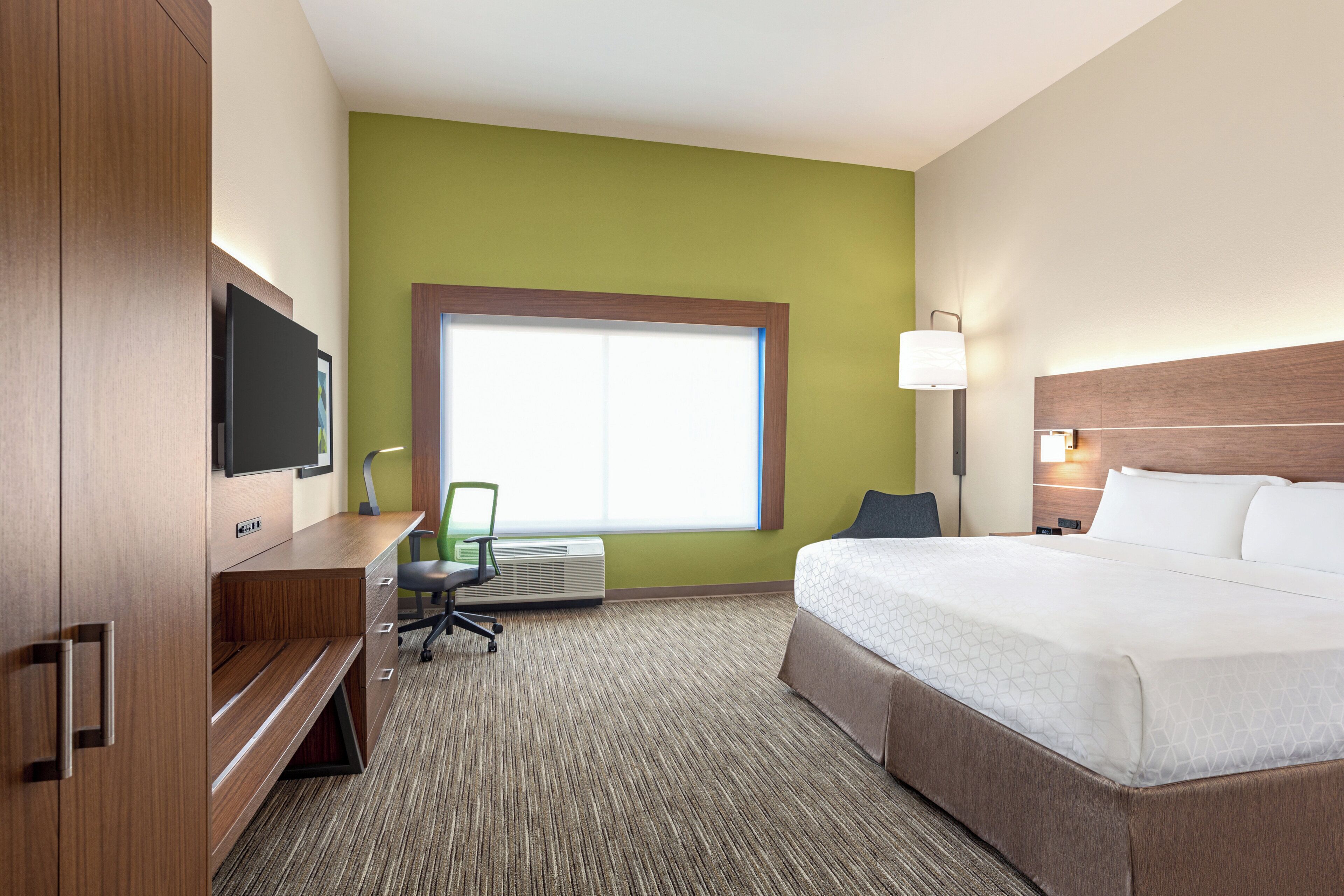 A hotel room with a bed, a desk, a chair, a television, and a window.