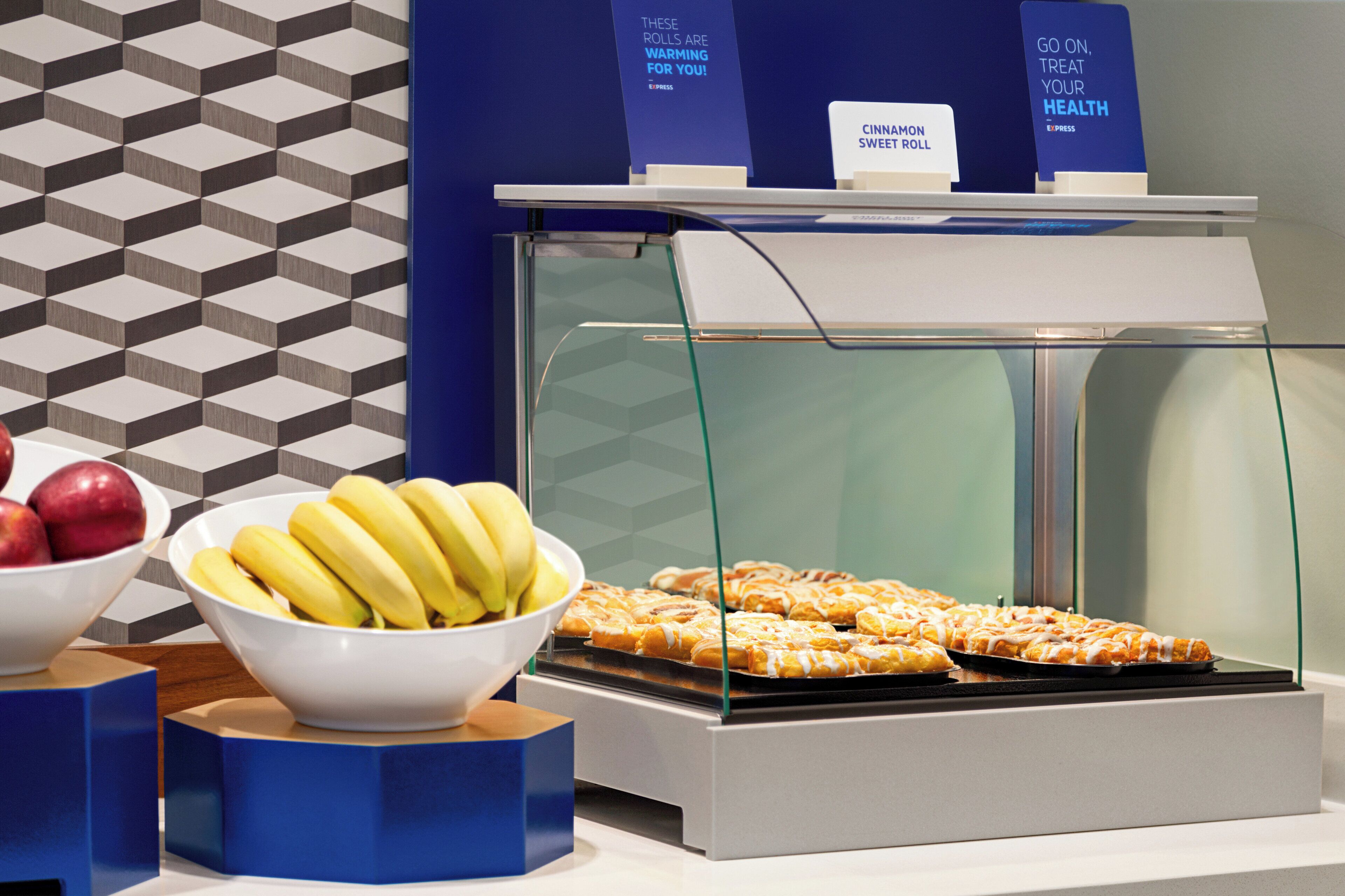 A buffet with a glass display case containing pastries and a bowl of bananas.