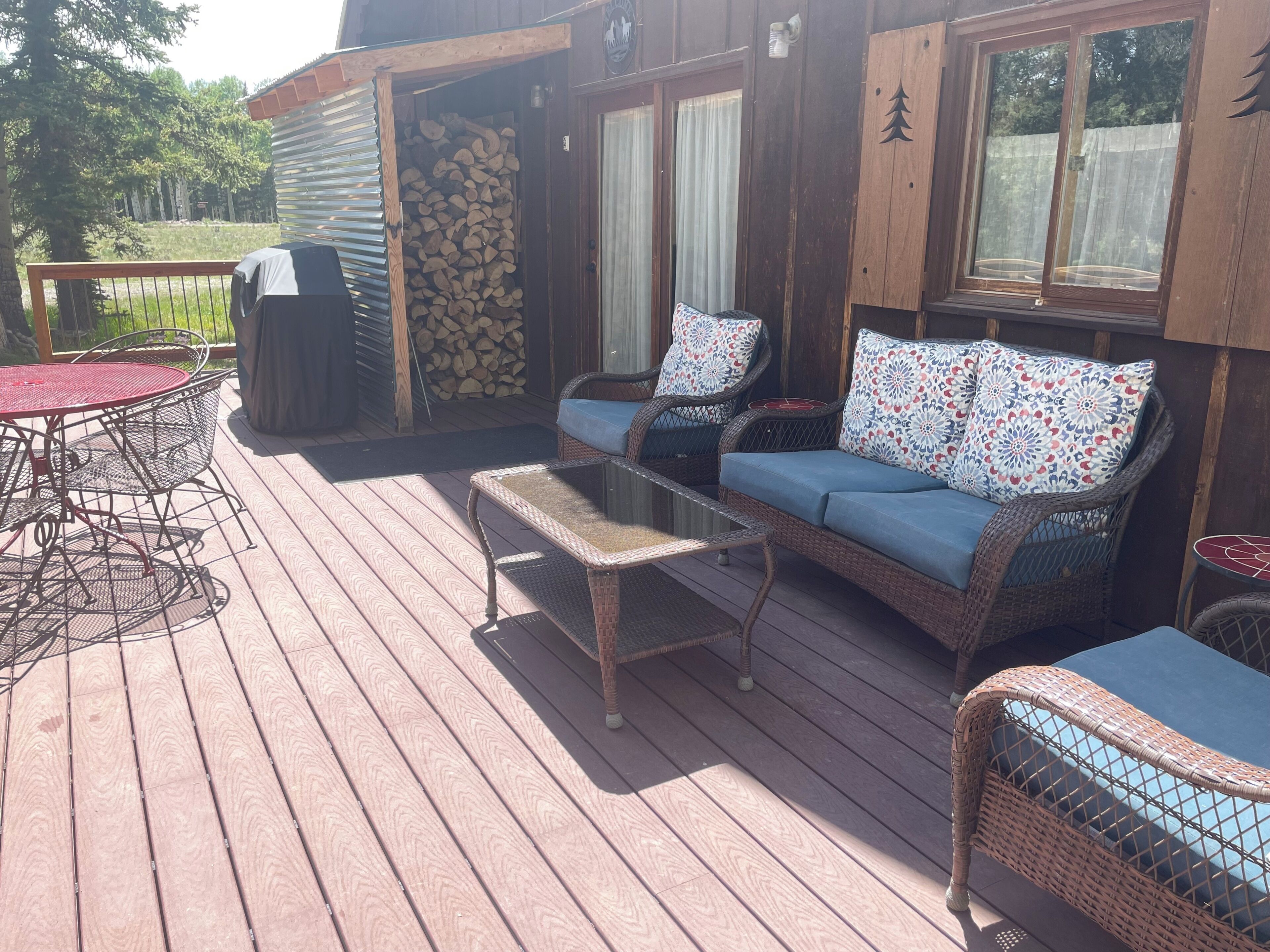 Een houten terras met rieten meubels, waaronder een bank en stoelen, en een kleine tafel.