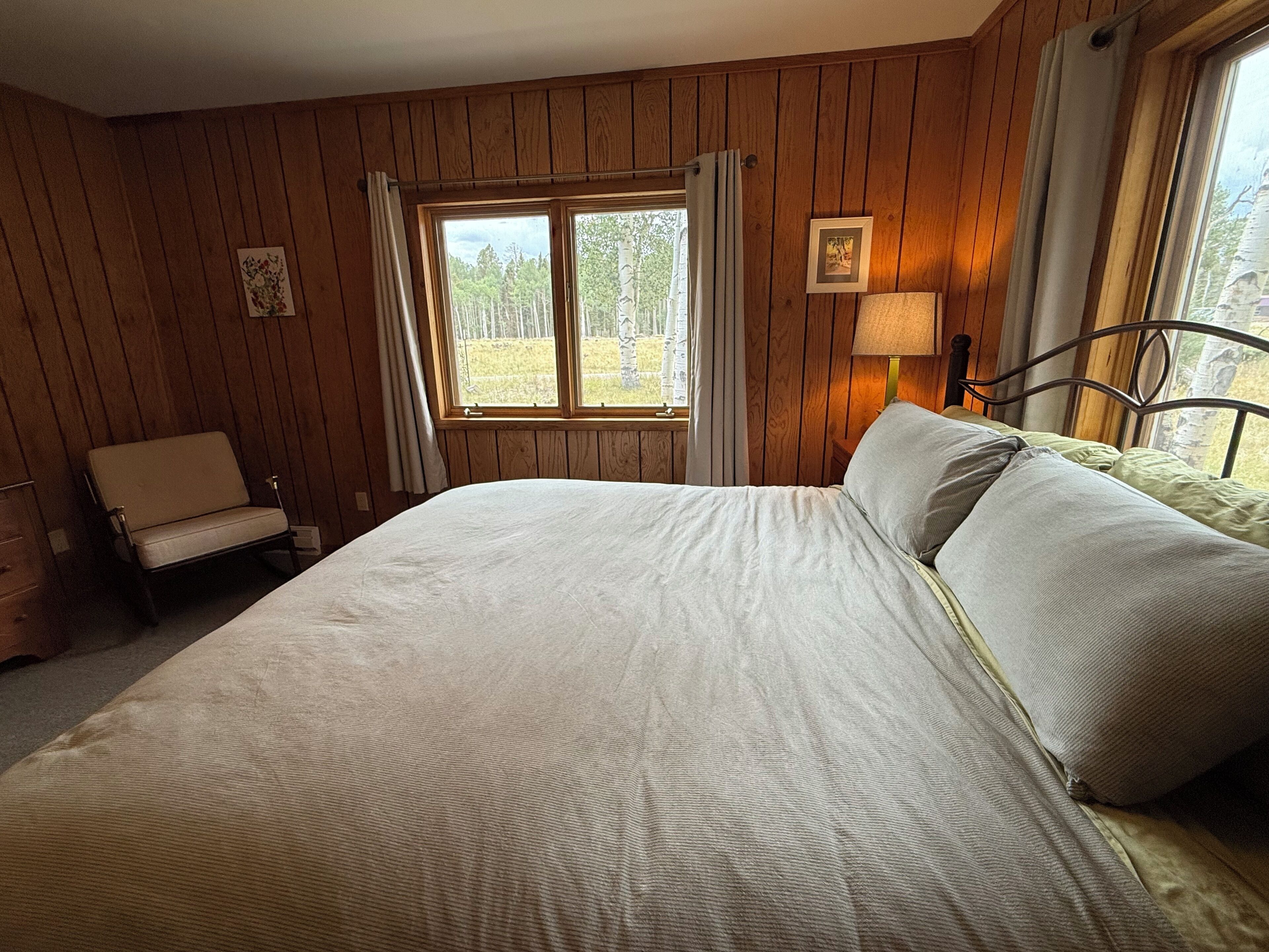 A bedroom with a large bed, a chair, a window with curtains, and a lamp.