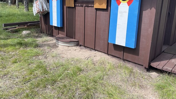 Een houten hutje met een golfplaten dak, een klein terras en een raam.