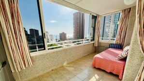 A bedroom with a large window, a bed, and a view of a cityscape.