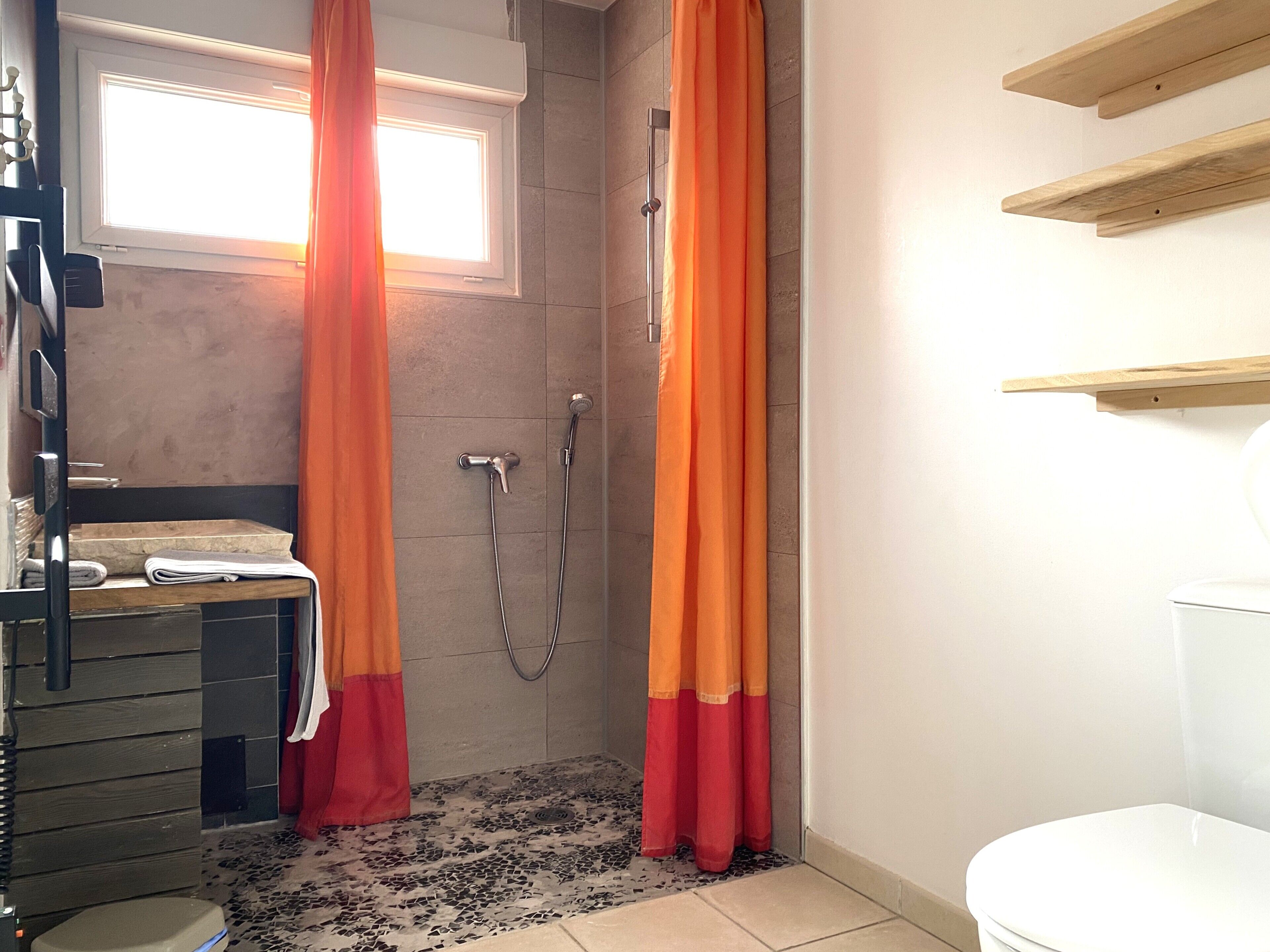 Een badkamer met een douche, toilet, wastafel en raam.