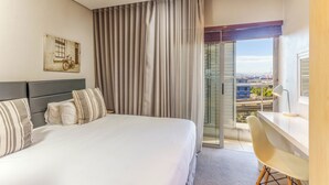 Habitación de hotel con cama, escritorio, silla, ventana con cortinas y un cuadro en la pared.