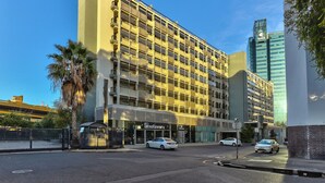 Un hotel de varios pisos con una fachada moderna, una entrada visible y un estacionamiento con coches.