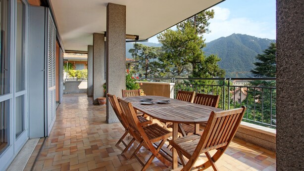 Un balcón con mesa y sillas de madera, piso de baldosas y vista a las montañas.