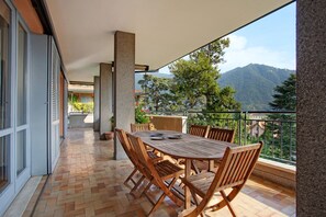 Ein Balkon mit Holztisch und -stühlen, einem Fliesenboden und Blick auf Berge.