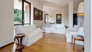 Un amplio salón con un sofá seccional blanco grande, una mesita redonda y vistas a través de un ventanal.