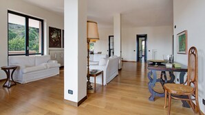 Amplia sala de estar con sofá, mesa y una silla. Se observa una ventana con vista a follaje.