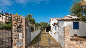 A stone pathway leading to a white building with a blue door, a metal gate, and a clear blue sky. - Vacation Home Casa Giovanna e Antonio with Sea View, A/C, Terrace & Garden (Calasetta)