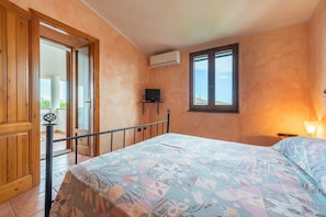 Un dormitorio con cama, televisor sobre un mueble, equipo de aire acondicionado y ventana.