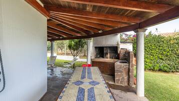 An outdoor patio with a tiled floor, a grill, and a covered area with wooden beams.