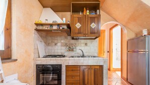 A compact kitchen with a gas stove, oven, and built-in dishwasher. There is a refrigerator and wooden cabinets above the sink. - Vacation Home Casa Giovanna e Antonio with Sea View, A/C, Terrace & Garden (Calasetta)