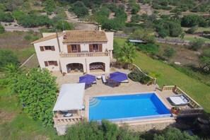 Una casa de dos pisos con piscina, mobiliario exterior y jardín.