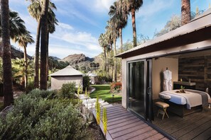 A spa room with a bed, a bench, and a view of a garden with palm trees and a mountain in the background. - Castle HOT Springs (MORRISTOWN)