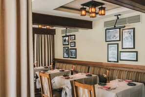 A restaurant with tables set for dining, framed pictures on the wall, and a wooden bench along the wall. - Castle HOT Springs (MORRISTOWN)