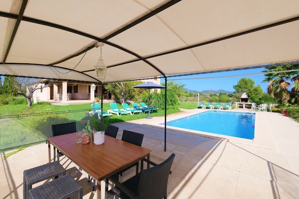 A covered patio with a pool, outdoor seating, and a view of the landscape.