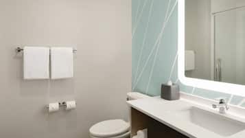 A modern bathroom with a toilet, two white towels, a sink, and a mirror.