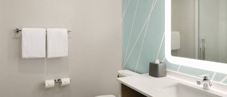 A modern bathroom with a toilet, two white towels, a sink, and a mirror.