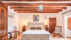 Un dormitorio con techo de madera, una cama con colcha blanca, una mecedora, un armario de madera y un cuadro en la pared.