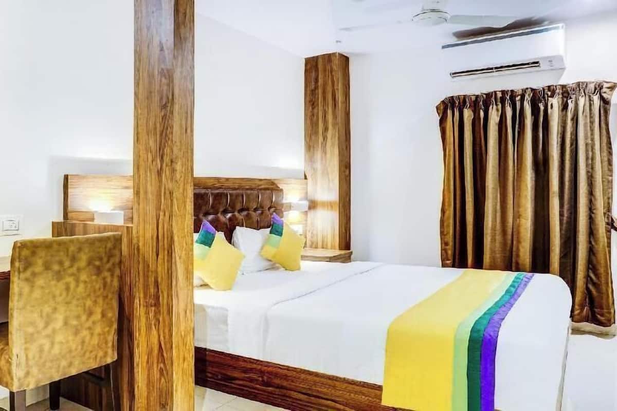 A hotel room with a wooden headboard, a bed with white bedding, a desk with a chair, and a window with curtains.