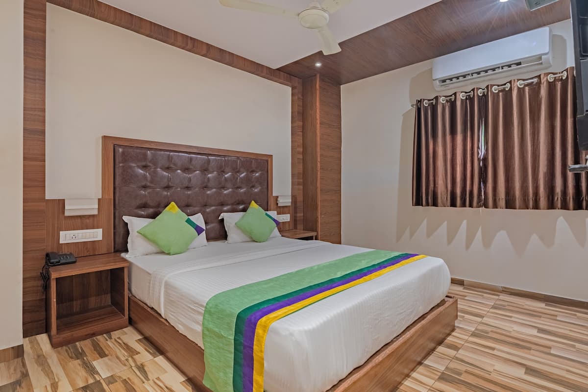 A bedroom with a tufted headboard, a wooden nightstand, a bedside table, a bed with a colorful blanket, and a window with curtains.