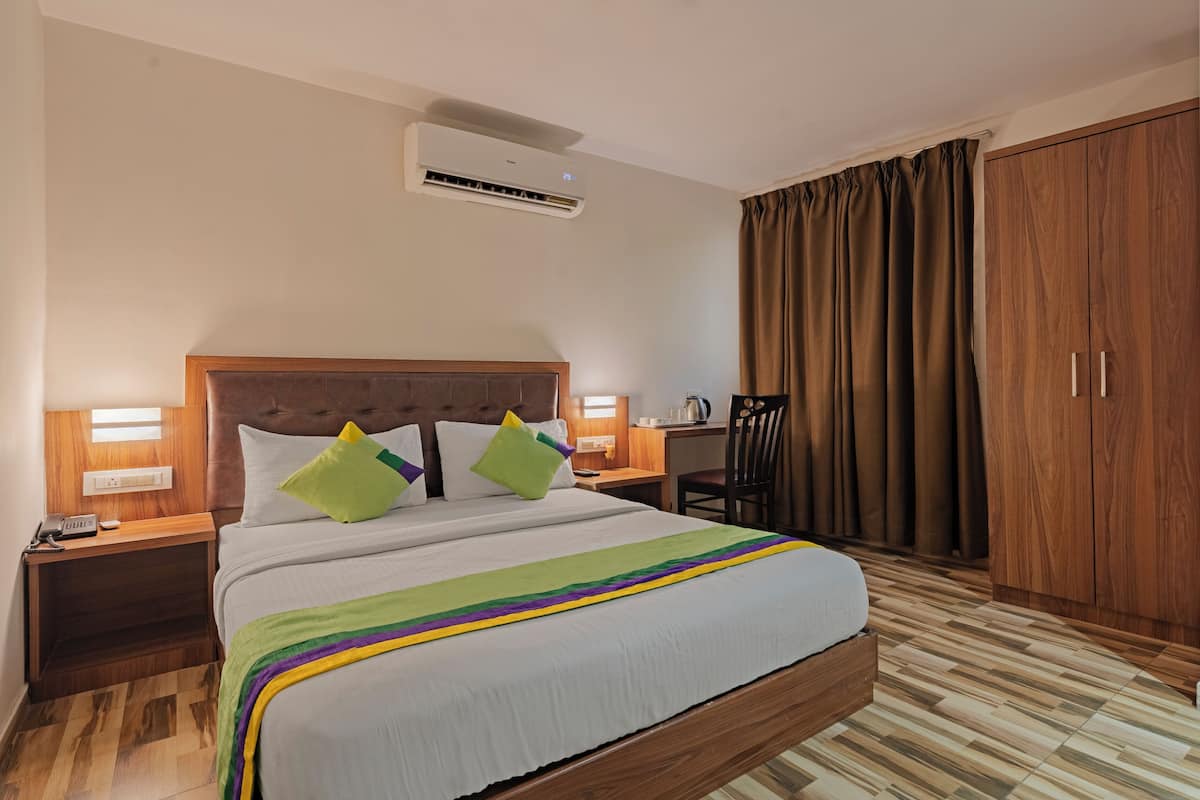 A hotel room with a bed, nightstands, a desk, a chair, an air conditioner, and a wardrobe.