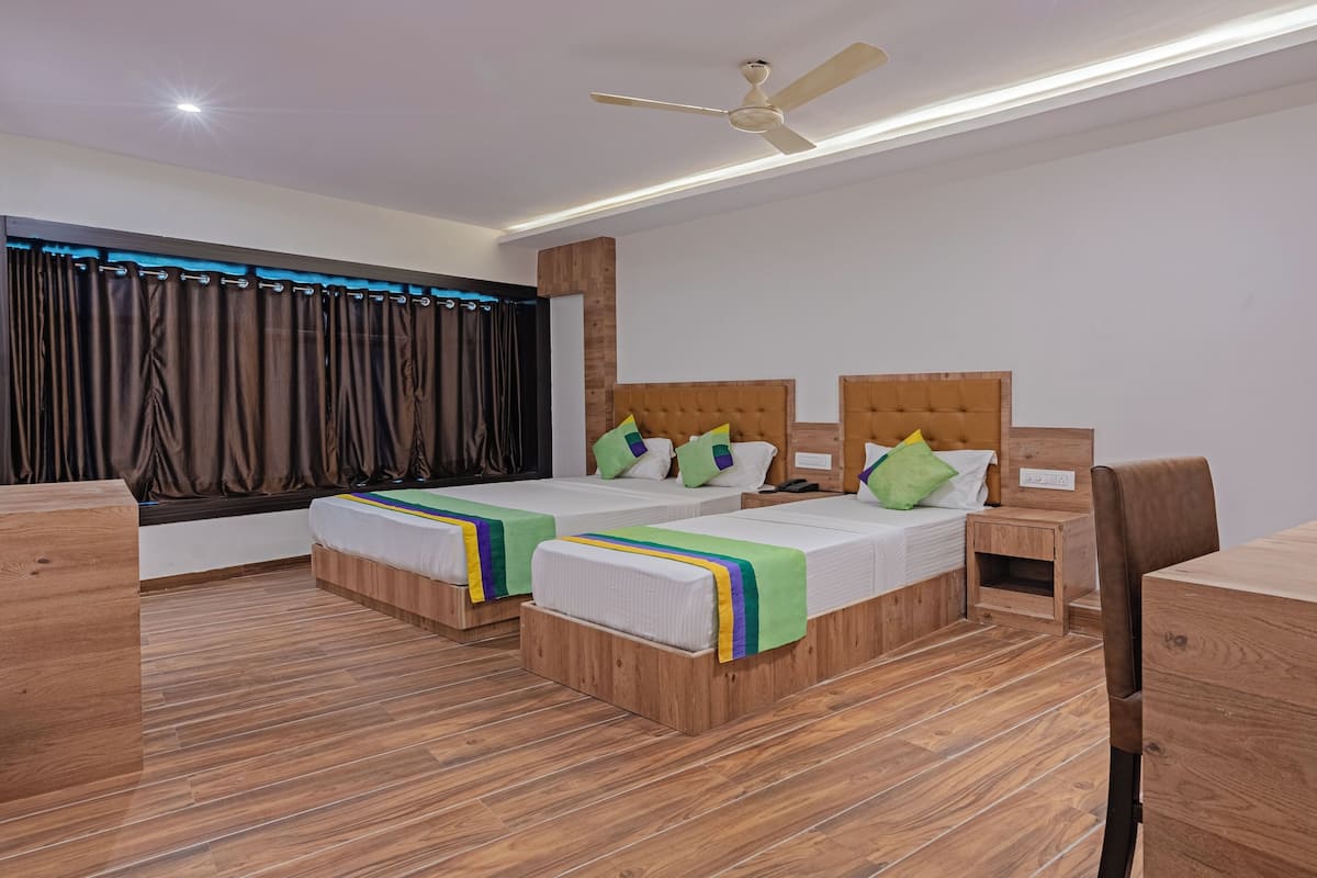 A hotel room with two beds, a wooden floor, a ceiling fan, and a desk with a chair.