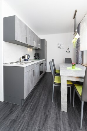 A modern kitchen with grey cabinets, a white countertop, and a dining area with a table and chairs.