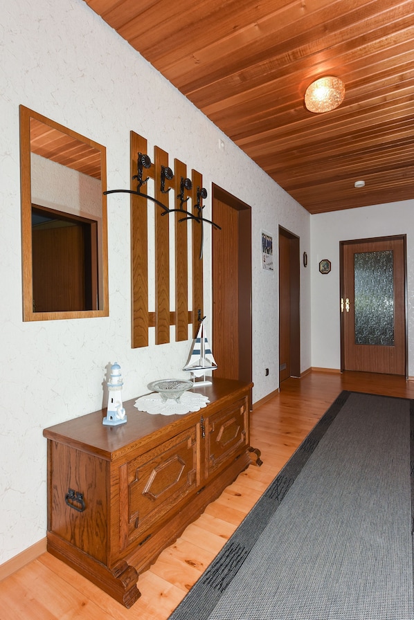 A hallway with wooden flooring, a wooden dresser with drawers, a mirror, and a door with a frosted glass panel.