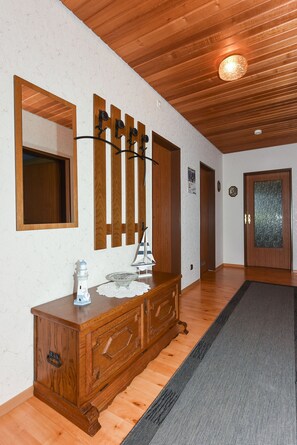 Ein Flur mit Holzboden, einem Holzkommoden mit Schubladen, einem Spiegel und einer Tür mit blickdichter Scheibe.