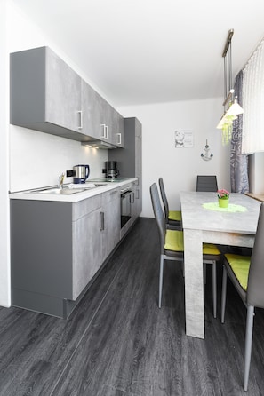 Una cucina moderna con mobili grigi, un piano di lavoro bianco e un'area pranzo con tavolo e sedie.