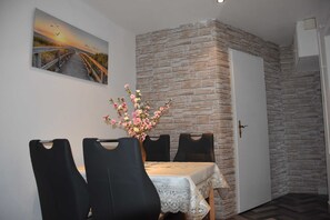 Uma sala de jantar com uma mesa posta para quatro pessoas, uma parede de tijolos decorativa, uma porta e um quadro na parede.