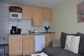 Cozinha compacta com armários de madeira, micro-ondas, cafeteira e lava-louças.