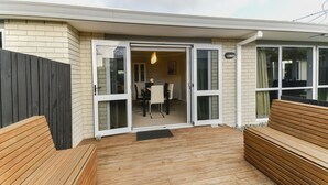 Eine Holzterrasse mit einer Bank, einem Essbereich mit Tisch und Stühlen sowie einer Glastür zum Innenraum.