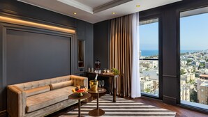 A modern living room with a sofa, a small round table with a fruit bowl, and a view of a cityscape through large windows. - Debrah Brown (Tel Aviv)