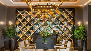 A lobby with a large, geometric bookshelf, two armchairs, a small table, and a chandelier. - Debrah Brown (Tel Aviv)
