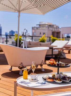 A rooftop terrace with a bathtub, dining table, and lounge chairs. - Debrah Brown (Tel Aviv)