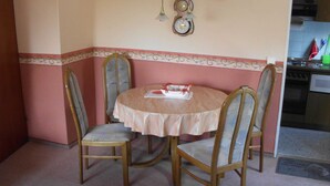 A dining area with a round table and four chairs, a clock on the wall, and a kitchen visible in the background. - Wohnung 73 - Hans-g. Otten (Wittmund)