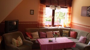 A living room with a sofa, armchair, and a television. There is a table with a pink tablecloth and a vase with flowers. - Wohnung 73 - Hans-g. Otten (Wittmund)