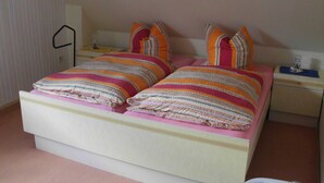 A bed with striped bedding and pillows, a bedside table with a lamp, and a nightstand with a small item on it. - Wohnung 73 - Hans-g. Otten (Wittmund)