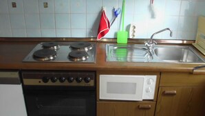 A kitchen with a stove, microwave, sink, and wooden cabinets. - Wohnung 73 - Hans-g. Otten (Wittmund)