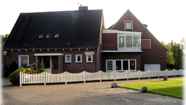 A two-story house with a brick facade, a white picket fence, and a garage. - Wohnung 73 - Hans-g. Otten (Wittmund)