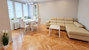 Moderni olohuone, jossa on beige sohva, valkoinen ruokapöytä tuoleineen ja pieni valkoinen pöytä.